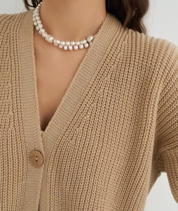 Detailed close-up of beige chunky knit cardigan with wood button and layered pearl necklace
