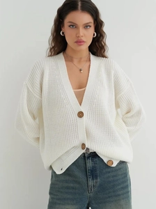 Detail of white chunky knit cardigan featuring a V-neck and three dark brown buttons