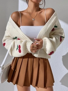 Detail shot of cherry embroidery on sleeve of cream knit cardigan and pleated skirt