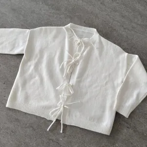 Detail of white knit cardigan showing elegant ribbon bow ties and soft ribbed textures