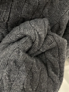 Detailed macro shot of dark grey thick cable knit wool sweater with rich fabric texture