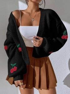 Detailed view of red cherry embroidery on the sleeve of a black chunky knit cardigan