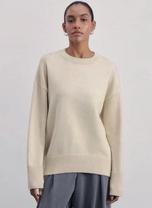 Detail of ribbed knit cuffs and hem on a loose beige crewneck sweater with drop shoulders