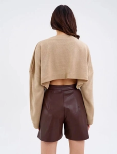 Detail showing the cropped back of a khaki cable knit sweater and brown faux leather shorts