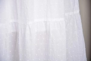 Dettaglio della texture in plumetis bianco con balze a strati su gonna a vita alta