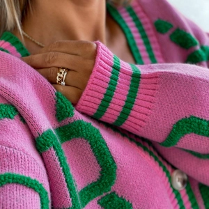 Close-up of pink knit cardigan with green stripe details and high-quality texture