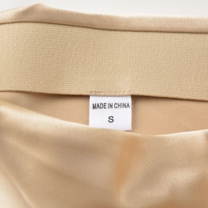 Détail macro de la jupe en satin champagne montrant l'étiquette de taille S et d'origine