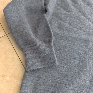 Gros plan des poignets côtelés du pull gris en tricot montrant la texture douce en laine