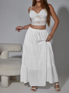 Dettaglio di gonna lunga a balze in plumetis bianco con coulisse e top in pizzo elegante
