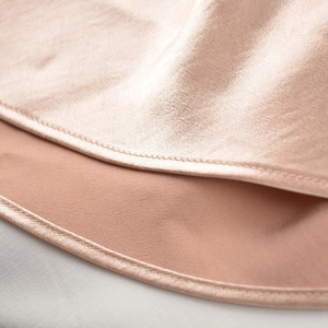 Detailed close-up of champagne satin fabric showing fine stitching and smooth pearlescent texture