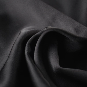 Gros plan sur un tissu satiné noir montrant une texture lisse et un élégant drapé soyeux