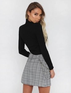 Close-up of ribbed long sleeve top and plaid skirt with stylish metal chain detail