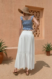 Full back view of a woman wearing a blue smocked top and tiered white maxi skirt outdoors