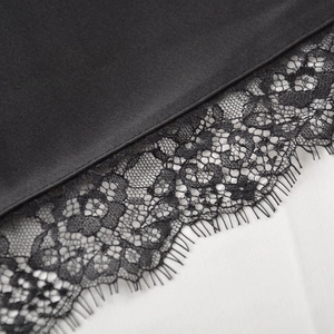 Détail de tissu satiné noir lisse avec bordure en dentelle florale délicate