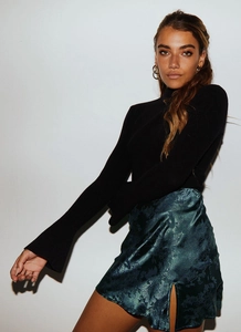 Détail de la jupe en satin vert foncé avec motifs floraux jacquard et fente latérale