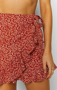 Detail of red floral wrap mini skirt with ruffle hem and side tie closure design