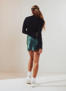 Vue arrière d'une mini-jupe en satin jacquard vert à taille haute et pull noir