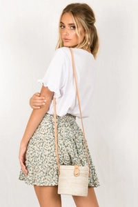 Detail of white ruffle sleeve t-shirt paired with green floral tiered mini skirt and woven bag