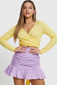 Detail of a wrap-style yellow ribbed top paired with a ruffled lavender mini skirt