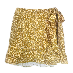 Macro view of wrap skirt showing yellow floral print, waist tie, and ruffle hem details