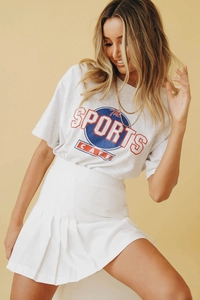 Détail d'un t-shirt gris avec logo vintage et d'une jupe plissée blanche à taille haute