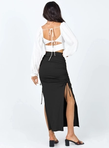 Rear view of white crop top with bow tie and black side drawstring slit maxi skirt