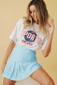 Détail d'une jupe plissée bleu clair à taille haute avec un t-shirt blanc de sport
