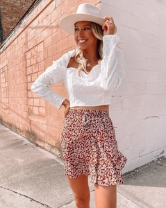 Detail of white long-sleeve jacquard top paired with a floral tiered mini skirt for summer