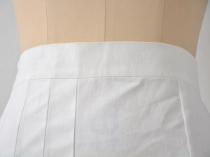 Détail de la taille haute d'une jupe plissée blanche montrant les coutures et le tissu sergé