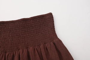 Detail of dark brown smocked elastic high waist and cotton-linen texture on long skirt