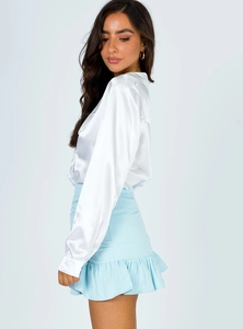 Close-up of white satin long sleeve shirt and light blue high waist ruffled mini skirt