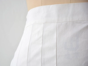 Vue détaillée de la taille haute et des plis soignés sur une jupe plissée blanche