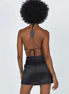 Detail view of the black satin backless halter top and matching mini skirt on model