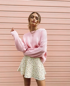 Pink knit sweater and floral mini skirt outfit shown in a natural street style setting