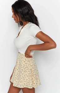 Side view of a woman wearing a white ribbed polo shirt and floral chiffon midi skirt