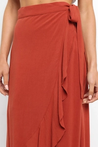 Detail of rust red chiffon wrap skirt featuring side ruffle trim and waist tie closure