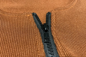 Macro shot of brown ribbed knit fabric with black zipper detail on slim fit top