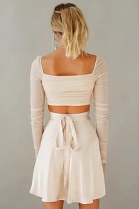 Detail eines beigen Satin-Wickelrocks mit Knotendetail und plissiertem Crop-Top Set