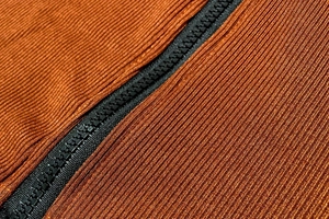 Detail of black zipper on dark orange ribbed knit fabric showing material texture