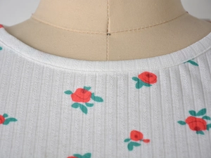 Detailed close-up of white ribbed knit top with red rose print and crew neckline design