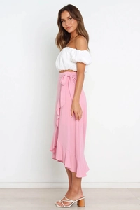 Detail of pink wrap skirt with tie waist and ruffled hem paired with a white off-shoulder top