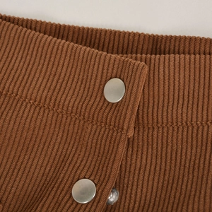 Macro detail of caramel corduroy fabric texture and silver metallic buttons on high waist
