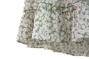 Close-up detail of green floral mini skirt featuring daisy print and ruffled hemline