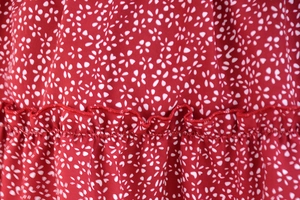 Macro shot of red floral chiffon fabric featuring ruffled hem stitching and precise sewing