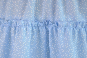 Detailed macro view of light blue floral chiffon fabric with ruffled edges and fine stitching