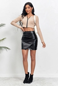 Détail d'une jupe asymétrique en similicuir noir avec un crop top en maille beige