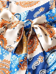 Macro detail of silk paisley print fabric with a decorative bow knot and orange floral motifs