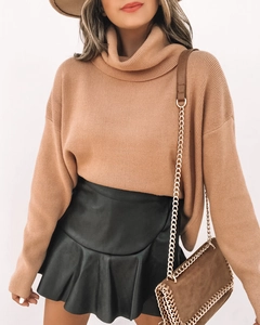 Détail d'une mini-jupe à volants en similicuir noir portée avec un pull en maille douce