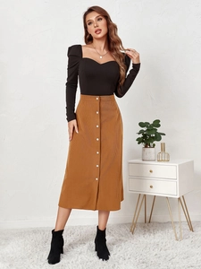 Detail of high waist brown corduroy skirt with white buttons and black long sleeve top