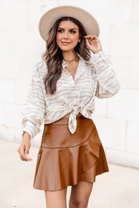 Détail de jupe en simili cuir caramel à volants et chemise beige nouée à motifs